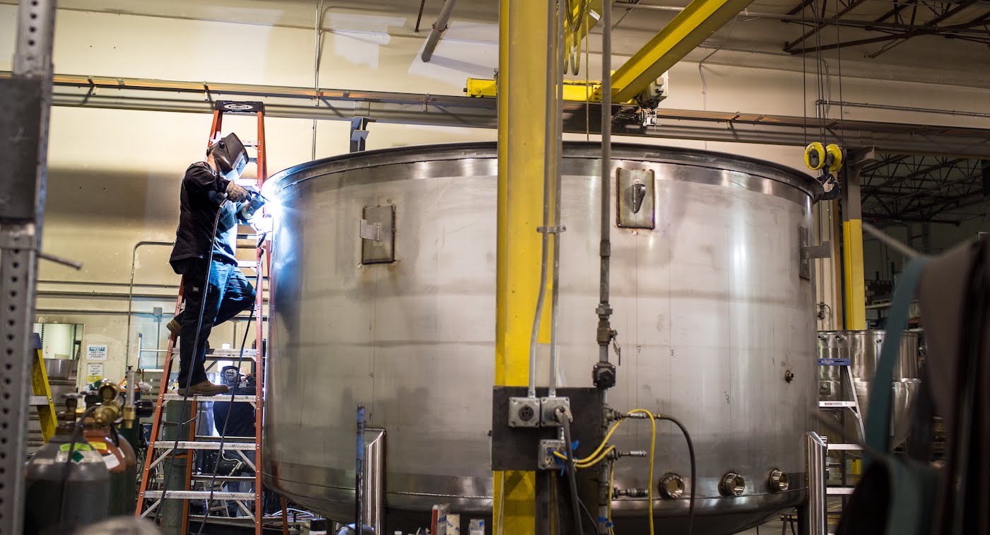 welder welding stainless steel tank in shop